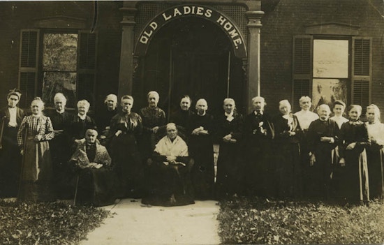A group of two dozen elderly women under a sign saying "Old Ladies Homes."