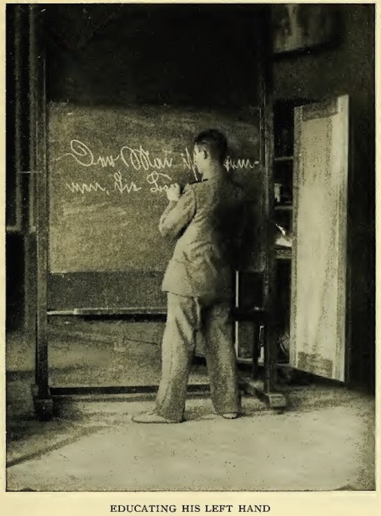 Man writing on a blackboard with his left hand.