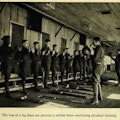 About a dozen one-legged men stand in a row, facing men holding exercise balls.  crutches lie on the floor.