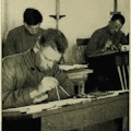 Three men sitting at desks, working with compasses.
