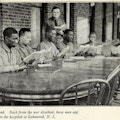 Six African American men sit around a table while a white man in uniform looks on.