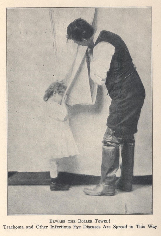 Small child dries hands and face with a roller towel also used by a man.