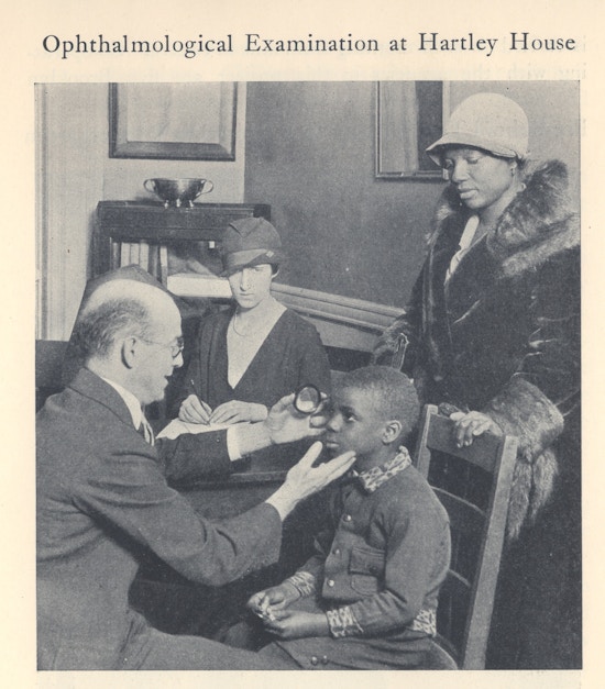 Doctor examines the eyes of an African American boy, two women look on.