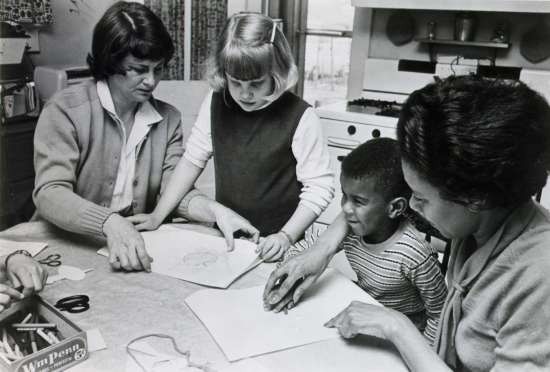 Two adults showing two children how to color.
