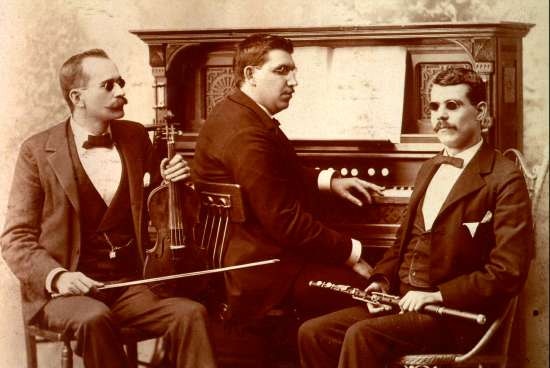Portrait of three blind musicians seated with their instruments -- a violin, a clarinet, and a piano.