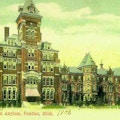 Color postcard of huge asylum in background with large courtyard in front