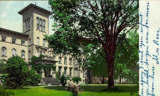 Color postcard of large building and lawn shaded by trees.