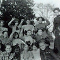 A group of younger students with their teacher pose outdoors.  Four of the girls finger spell Alabama