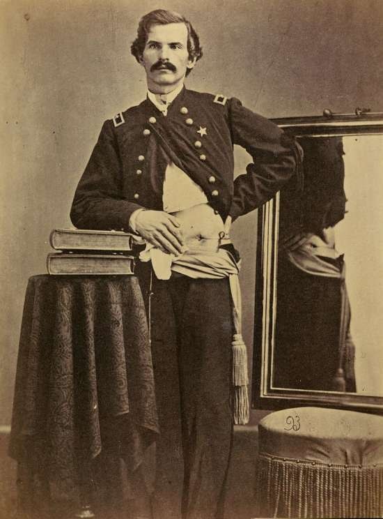 Henry Barnum in uniform.  His coat and shirt are pulled aside from his left hip revealing a wound through which a string passes.