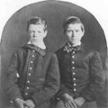 Photograph of two young boys with buttoned coats and bow ties.