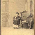 Chinese man of small stature stands with one arm on a chair.