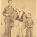 Chang and Eng stand between a young man and a boy.