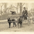 Two dogs pull a man on a wagon. A cannon is in the background.