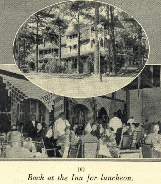 A large wooden building among trees and people sitting down for lunch.