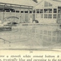 A swimming pool with an umbrella and glassed building in the background.