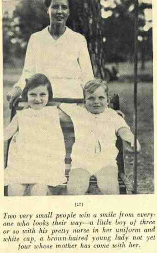 Two children sit in a swing with a nurse standing behind them.