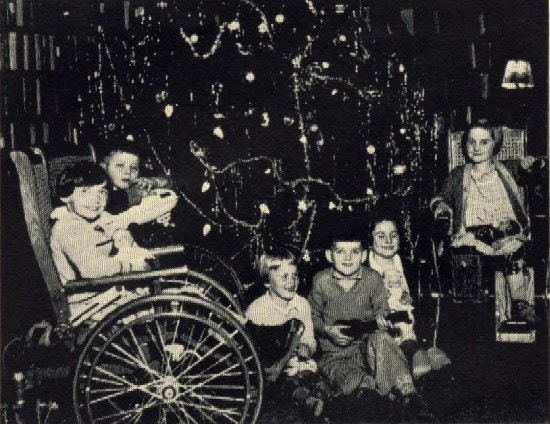 Children, three in wheelchairs, around a decorated Christmas tree.