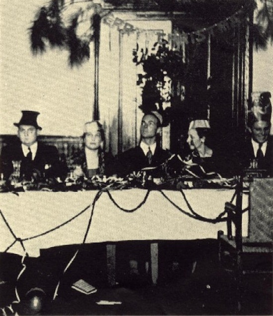 Three man and two women in strange hats sit at a table.
