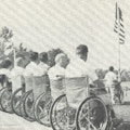 A row of men in wheelchairs before an American flag.