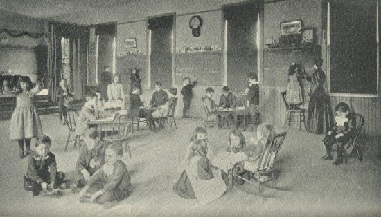 Childern in a large room, some sitting and others standing.