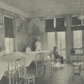 A hospital ward with three boys in beds, one boy sitting, and anurse standing.