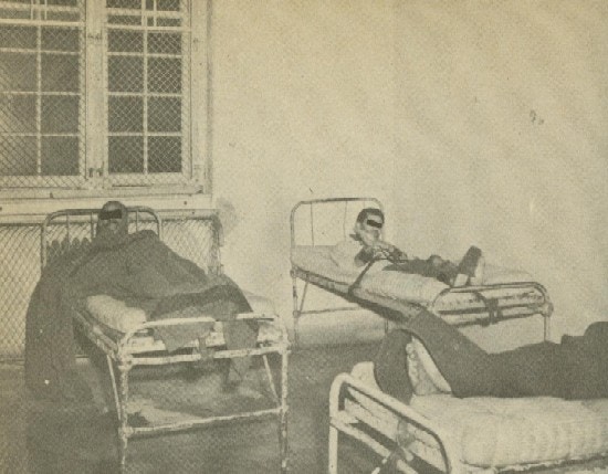 Three men restrained in beds.