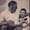 A father with his arm around his son, both holding cold drinks.
