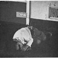 An African-American boy lying on the floor next a metal door.