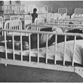 A child lying in bed with side rails in a room filled with identical beds.