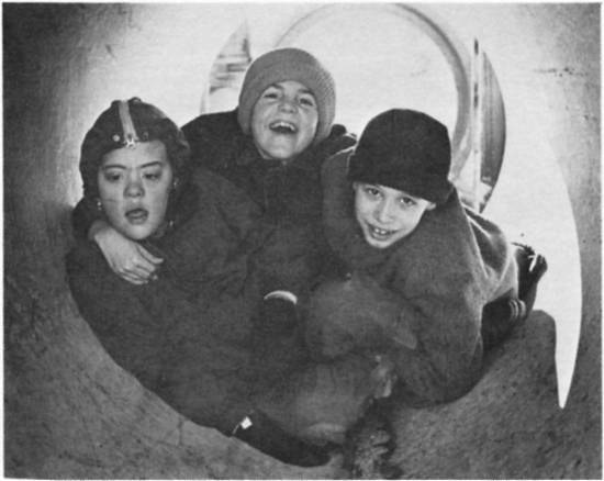 Three boys playing inside large pipe.