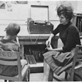 A boy, in a chair marked Fred, sits next to a woman and a record player.