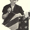 An elderly woman sewing an American flag.