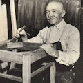 An elderly man varnishing a chair.