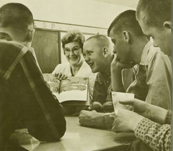 A woman showing a Dr. Seuss book to four teenage boys.