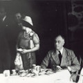 FDR sits at a table next a standing Queen Elizabeth.