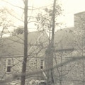 A stone house during construction, seen through trees.