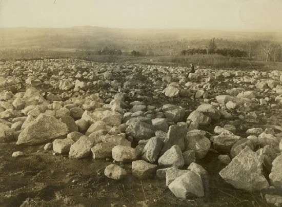 A single young man looks upon a field of recently cleared large rocks.