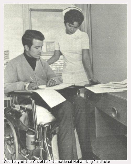 A man in a wheelchair and a nurse look at papers.
