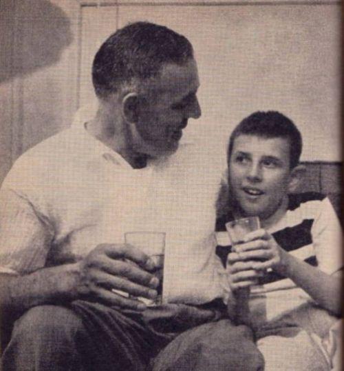 A father with his arm around his son, both holding cold drinks.