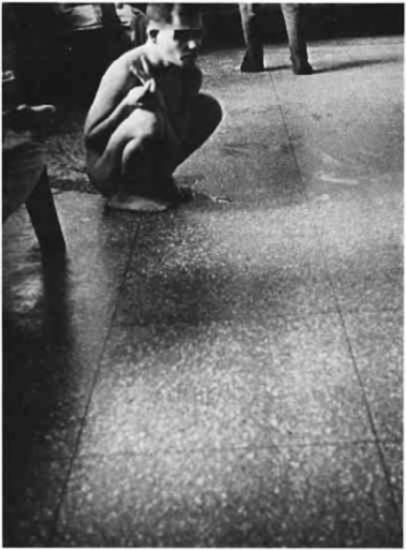 A naked young man crouching on a stone floor.