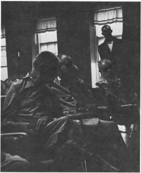 Men on a ward, one stands near a window.