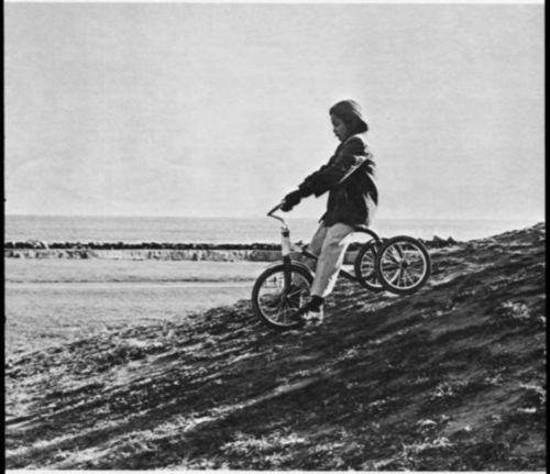 A boy riding down a hill on a tricycle.