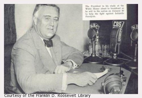 FDR sits at desk with CBS and NBC radio microphones.