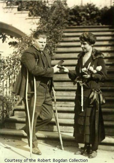 Mrs. Coolidge presents a medal to a man (L.B. Clark) on crutches.