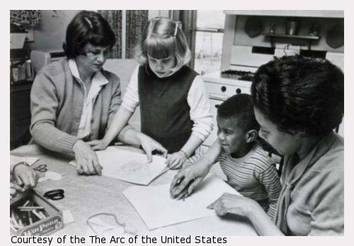 Two adults showing two children how to color.