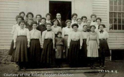 Photograph of girls and male teacher on front steps of school building.  One of the girls is short-statured.