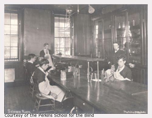 male students seated around table with science experiments, holding chemistry beakers.