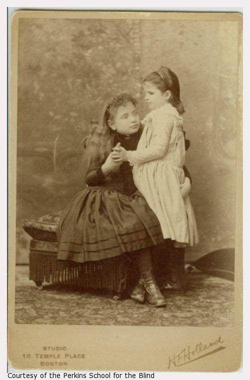 Helen Keller as a young child, sitting, holding a younger child's hand standing to her left.