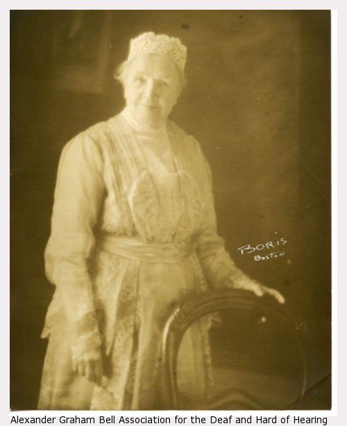 Sarah Fuller standing, with hand on chair.