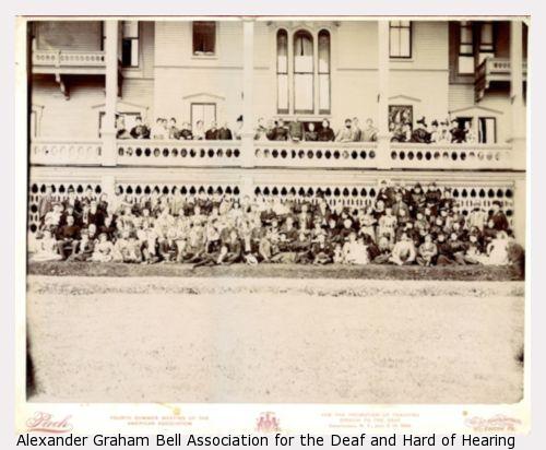 Large group photograph of American Association To Promote Teaching Speech To The Deaf summer meeting attendees wrapped above and below a large white porch in 1894.